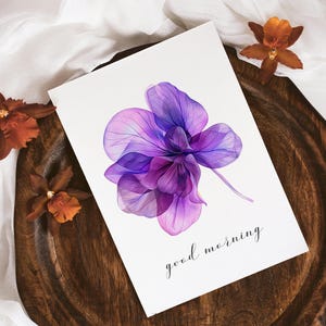 May include: A watercolor painting of a purple orchid with a translucent effect. The painting is on a white card with the text "good morning" written in black ink.