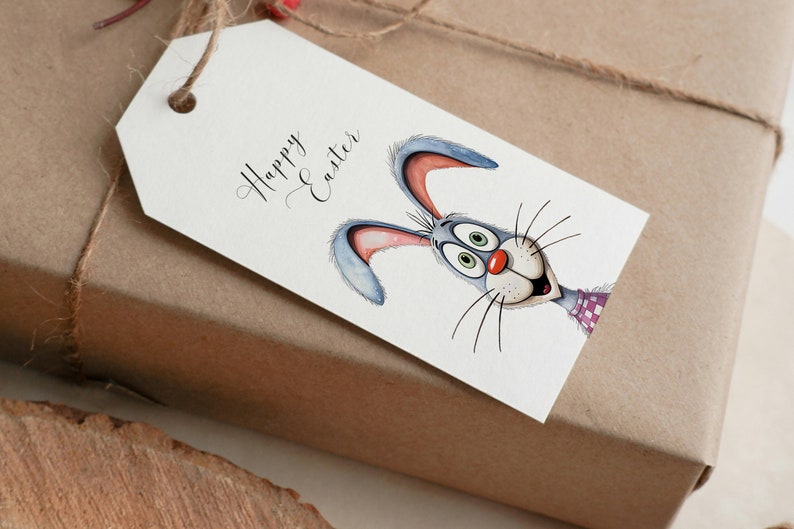 May include: A white gift tag with the text "Happy Easter" in black cursive script. A cartoon bunny with blue ears, green eyes, and a red nose is peeking out from behind the text.