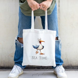 K&ouml;nnte beinhalten: Wei&szlig;e Stofftasche mit einer Cartoon-M&ouml;wen-Illustration und dem Text "SEA TIME".