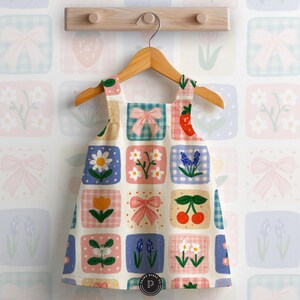 Puede incluir: Un vestido sin mangas con un patr&oacute;n de cuadr&iacute;cula de cuadrados coloridos. Cada cuadrado contiene una ilustraci&oacute;n &uacute;nica, incluyendo lazos rosas, fresas rojas, cerezas, margaritas blancas, tulipanes naranjas y flores azules sobre un fondo crema.
