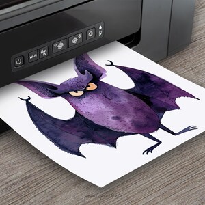 Puede incluir: Una ilustraci&oacute;n de acuarela morada de un murci&eacute;lago con ojos grandes y enojados. El murci&eacute;lago est&aacute; impreso en una hoja de papel blanca que sale de una impresora negra.