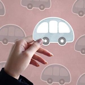 May include: A hand holds up a light blue paper car cutout against a pink background with a pattern of gray paper car cutouts.