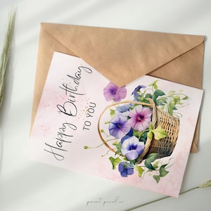 Op de afbeelding: Een roze kaart met de tekst "Happy Birthday to You" in zwarte cursieve letters. De kaart heeft een aquarel-illustratie van een rieten mand vol met paarse en blauwe bloemen.