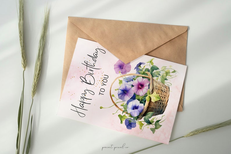 Op de afbeelding: Een roze kaart met de tekst "Happy Birthday to You" in zwarte cursieve letters. De kaart heeft een aquarel-illustratie van een rieten mand vol met paarse en blauwe bloemen.