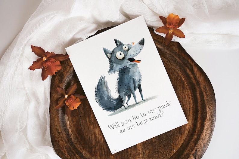 Puede incluir: Una tarjeta blanca con una ilustraci&oacute;n de lobo de dibujos animados y el texto "Will you be in my pack as my best man?" El lobo tiene un cuerpo azul gris&aacute;ceo, una cara blanca y ojos grandes y redondos. La tarjeta est&aacute; sobre una superficie de madera con un pa&ntilde;o blanco y flores naranjas.