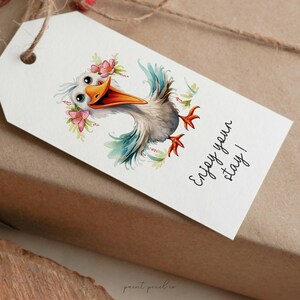 K&ouml;nnte beinhalten: Ein wei&szlig;er Geschenkanh&auml;nger mit einer Cartoon-Illustration eines Vogels, der eine Blumenkrone tr&auml;gt. Der Text auf dem Anh&auml;nger lautet "Genie&szlig;en Sie Ihren Aufenthalt!"