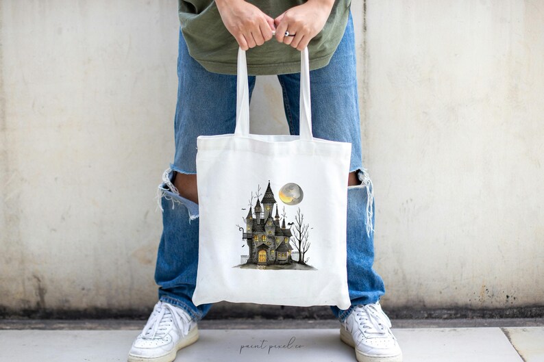 May include: A white tote bag with a black and white illustration of a haunted house with a full moon. The house has windows and a door with a light shining from inside.