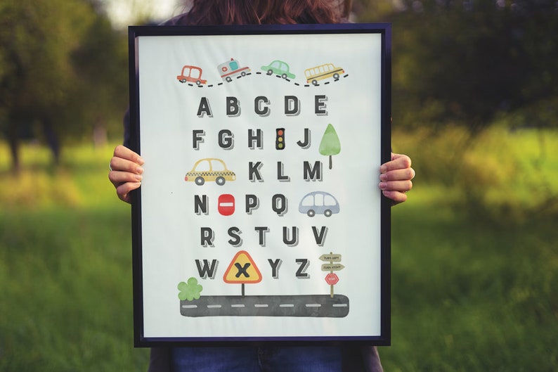 May include: A white framed alphabet chart with a road theme. The letters are in black and are surrounded by various road signs and vehicles, including a school bus, ambulance, taxi, and stop sign. The letters are A-Z.
