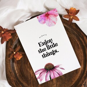 K&ouml;nnte beinhalten: Eine wei&szlig;e Karte mit dem Text "ALWAYS Enjoy the little things." in Schwarz gedruckt. Die Karte ist mit rosa und violetten Aquarellblumen verziert und liegt auf einer Holzoberfl&auml;che.