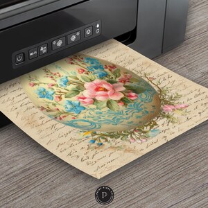 May include: A printed image of a decorative Easter egg with a floral design, featuring pink and blue flowers on a cream-colored background. The egg is printed on aged paper with handwritten script. A black printer is in the background.