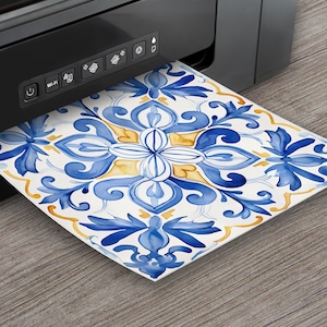 May include: A black printer is shown printing a square tile design. The tile features a watercolor floral pattern in shades of blue and yellow on a white background. The design is emerging from the printer.