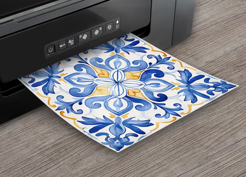 May include: A black printer is shown printing a square tile design. The tile features a watercolor floral pattern in shades of blue and yellow on a white background. The design is emerging from the printer.