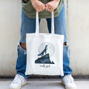 Puede incluir: Bolsa de tela blanca con un lobo aullando a la luna y el texto "wolf girl".