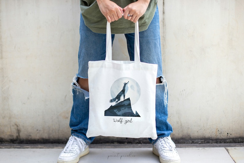 Puede incluir: Bolsa de tela blanca con un lobo aullando a la luna y el texto "wolf girl".