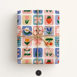 Puede incluir: Un regalo rectangular envuelto en papel con una cuadr&iacute;cula de cuadrados con ilustraciones de lazos rosas, fresas rojas, cerezas y varias flores, incluyendo tulipanes y margaritas, atado con un cordel marr&oacute;n fino en forma de lazo.