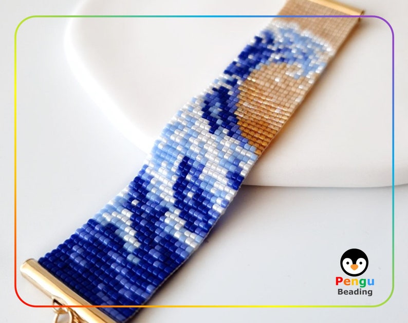 K&ouml;nnte beinhalten: Ein blaues und wei&szlig;es Perlenarmband mit einem goldenen Verschluss. Das Armband zeigt ein Design, das von der Gro&szlig;en Welle vor Kanagawa inspiriert ist, einem ber&uuml;hmten japanischen Holzschnitt. Das Armband ist von Pengu Beading hergestellt.