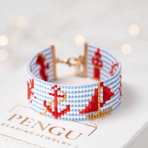 May include: A blue and white striped beaded bracelet with red and gold accents. The bracelet features a nautical theme with images of sailboats, anchors, and lighthouses.