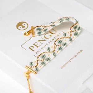 Op de afbeelding: Een witte en groene kralen armband met gouden accenten en een gouden sluiting. De armband ligt op een witte doos met de tekst "PENGU Beading Jewelry" en "charming things inside".