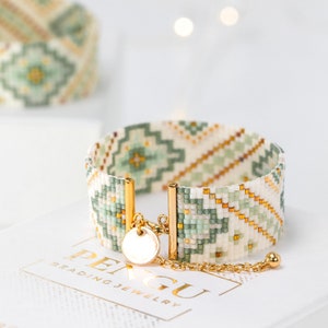 Peut inclure: Un bracelet en perles blanches, vertes et dorées avec un motif géométrique. Le bracelet a un fermoir doré et un petit charme doré.
