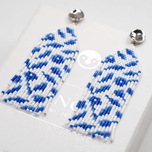 May include: A pair of long, blue and white beaded earrings with silver hooks. The beads are arranged in a geometric pattern.