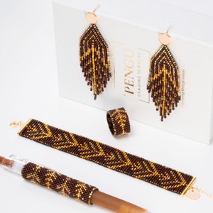 Könnte beinhalten: Ein Set aus braunem und goldenem Perlen-Schmuck, bestehend aus einem Armband, einem Ring und Ohrringen. Der Schmuck hat ein geometrisches Muster und wird von Pengu Beading Jewelry hergestellt.