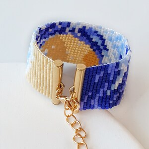 K&ouml;nnte beinhalten: Ein Armband aus Perlen mit einem blauen und wei&szlig;en Muster und einem goldenen Verschluss. Das Armband besteht aus kleinen Perlen und hat eine Kette, die am Verschluss befestigt ist.