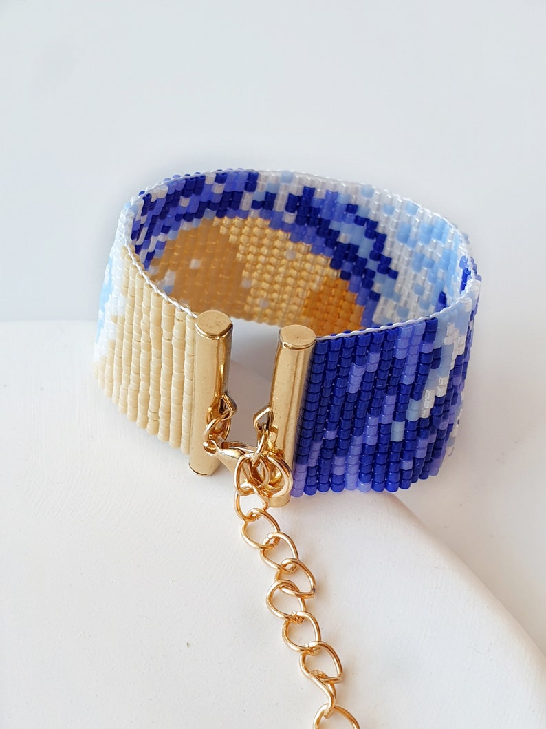 K&ouml;nnte beinhalten: Ein Armband aus Perlen mit einem blauen und wei&szlig;en Muster und einem goldenen Verschluss. Das Armband besteht aus kleinen Perlen und hat eine Kette, die am Verschluss befestigt ist.