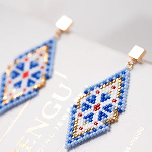 May include: A pair of blue, white, and red beaded earrings with gold accents. The earrings are shaped like diamonds and have a geometric pattern.