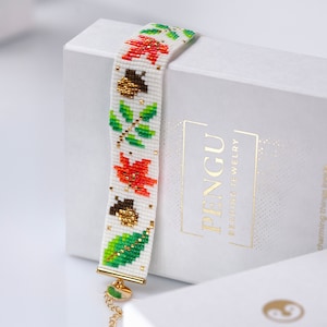 May include: A white beaded bracelet with a pattern of green leaves, orange and red maple leaves, and brown acorns. The bracelet is on a white box with the text "PENGU BEADING JEWELRY" in gold lettering.