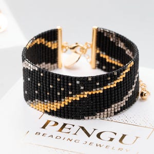 May include: Black beaded bracelet with gold and silver accents. The bracelet has a clasp closure and a small gold bead at the end of the chain.