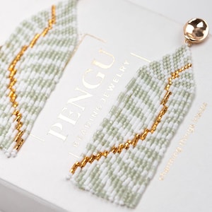 May include: A pair of long, beaded earrings with a white and light green color scheme. The earrings feature a gold accent and are displayed on a white box with the text "PENGU BEADING JEWELRY" and "charming things inside".
