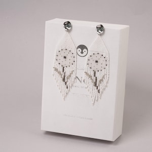 May include: White beaded earrings with a floral design and silver accents. The earrings are displayed on a white card with the text "No" and "ing Jew".
