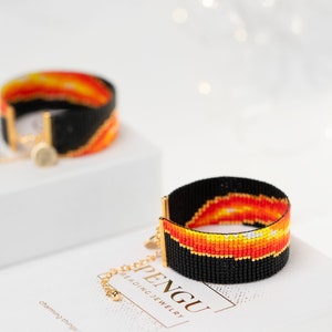 May include: Two beaded bracelets with a black background and a colorful design of orange, yellow, and white. The bracelets are on a white surface with the text "PENGU BEADING JEWELRY" and "charming things" visible.