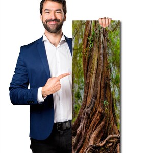 May include: A vertical print of a tree trunk, 12 x 36 inches, with rough, textured bark and exposed roots. The background shows green foliage. The print is held by a person wearing a blue blazer and black pants.