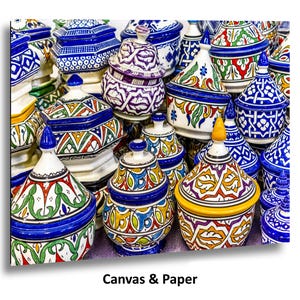 May include: A selection of brightly coloured ceramic tagine pots, each with unique patterns and designs. The pots display a variety of colours, including blue, green, yellow, and red, with detailed geometric and floral motifs. The text "Canvas & Paper" is at the bottom.