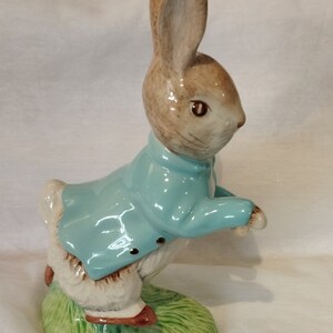Peut inclure: Une figurine en céramique de Lapin de Pâques portant une veste bleue et debout sur une base verte.