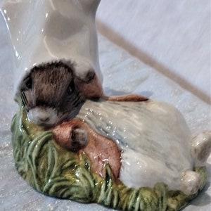 Peut inclure: Une figurine en céramique d'un lapin portant un bonnet blanc et allongé sur un lit d'herbe verte. Le lapin tient une carotte dans ses pattes.