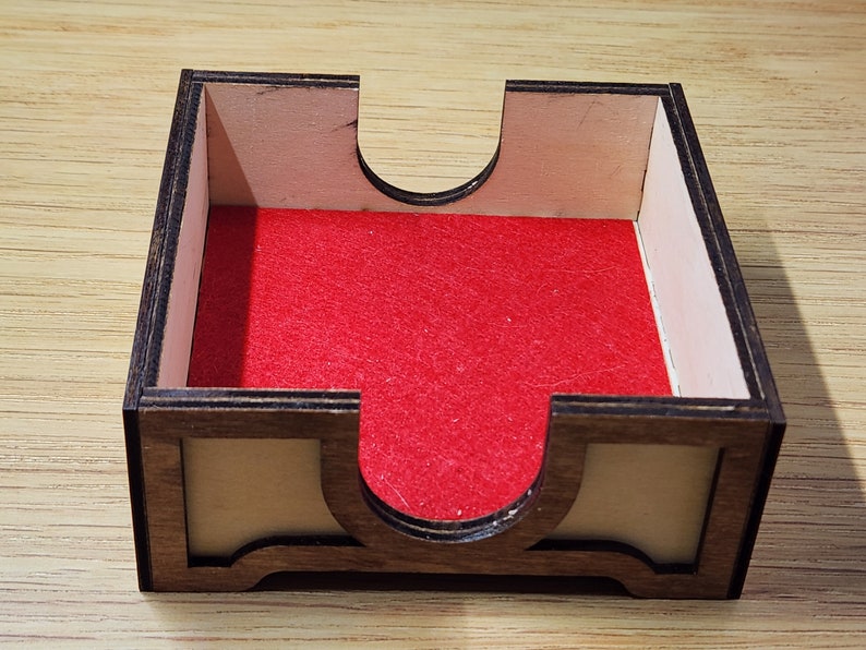 Puede incluir: Una bandeja de dados de madera con un forro de fieltro rojo. La bandeja tiene una secci&oacute;n elevada en el centro para evitar que los dados se salgan.