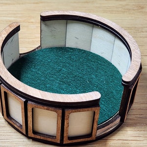 Pu&ograve; includere: Un vassoio per dadi in legno con un rivestimento in feltro verde e un bordo decorativo. Il vassoio ha otto scomparti attorno al bordo.
