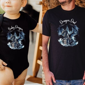 May include: A black t-shirt with a dragon graphic and the text "Baby Dragon" on the front. A black t-shirt with a dragon graphic and the text "Dragon Dad" on the front.