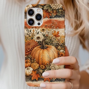 May include: A smartphone case featuring a detailed autumn-themed illustration of a large central pumpkin surrounded by various orange, yellow, and white chrysanthemums, small wildflowers, and scattered maple leaves against a textured background.