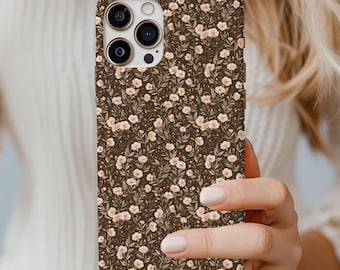Könnte beinhalten: Eine Smartphone-Hülle mit dunkelbraunem Hintergrund und einem sich wiederholenden Muster aus kleinen, hellrosa Blüten und grünem Blattwerk. Die Hülle verfügt über einen Ausschnitt für ein Dreifach-Kamerasystem und einen Blitz.