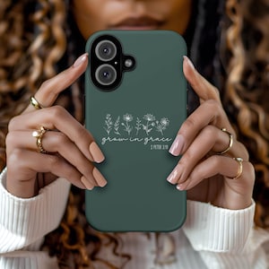 May include: A dark green phone case with a camera and the words "grow in grace" and "2 Peter 3:18" in white script. The case features a floral design. The phone case is held by a person.