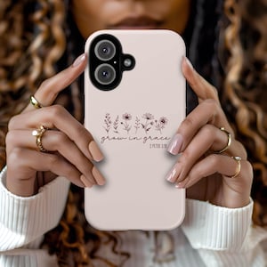 May include: A light pink phone case featuring a floral design and the words "grow in grace" with the scripture reference 2 Peter 3:18. The case has a dual-lens camera cutout.