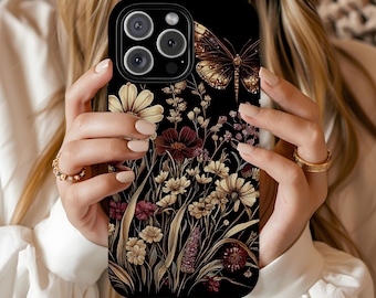 May include: Black phone case featuring a floral design with a butterfly. The case has a detailed illustration of flowers in shades of cream, burgundy, and gold. The butterfly is in the upper right corner. The phone case is held by a person.