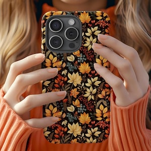 May include: A smartphone case featuring a repeating pattern of autumn leaves, berries, and foliage in shades of yellow, orange, and deep red set against a black background. The case has a cutout for a triple-lens camera system on the top left.
