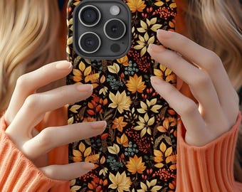 May include: A smartphone case featuring a repeating pattern of autumn leaves, berries, and foliage in shades of yellow, orange, and deep red set against a black background. The case has a cutout for a triple-lens camera system on the top left.