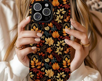 May include: A black phone case featuring a colorful autumn leaf pattern. The design includes orange, yellow, and green leaves, along with red berries, set against a dark background. The case has a glossy finish and a camera cutout.