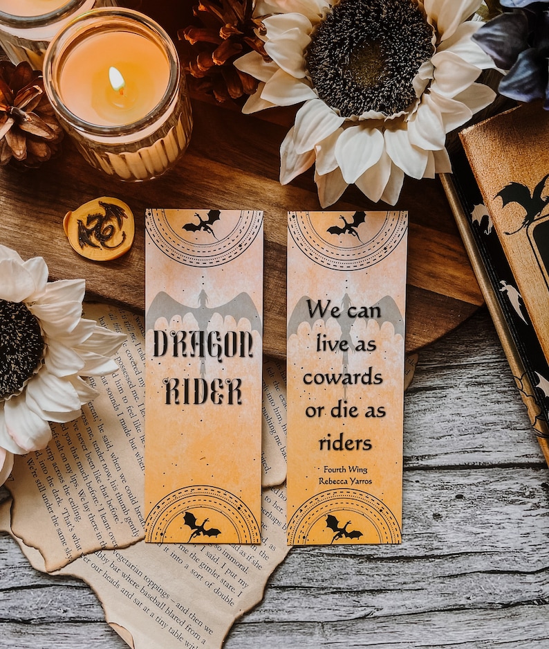 May include: Two orange and black bookmark designs with dragon illustrations and quotes. The first bookmark says "Dragon Rider" and the second bookmark says "We can live as cowards or die as riders. Fourth Wing, Rebecca Yarros."