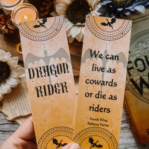 May include: Two yellow bookmark designs with black dragon silhouettes and text. The first bookmark says "DRAGON RIDER". The second bookmark says "We can live as cowards or die as riders - Fourth Wing Rebecca Yarros".